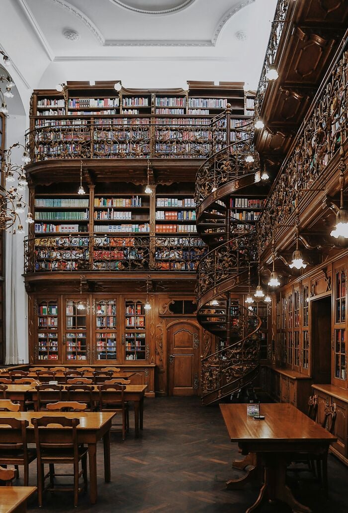 Grandiose Bibliothekseinrichtung mit Holzregalen, Wendeltreppe und gem&uuml;tlichen Lesetischen voller B&uuml;cher aus aller Welt.