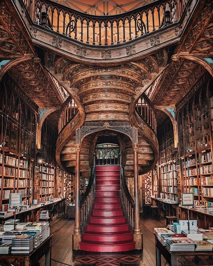 Libreria sfarzosa e imponente con una scalinata a chiocciola intagliata in legno e file di scaffali pieni di libri tutt'intorno.
